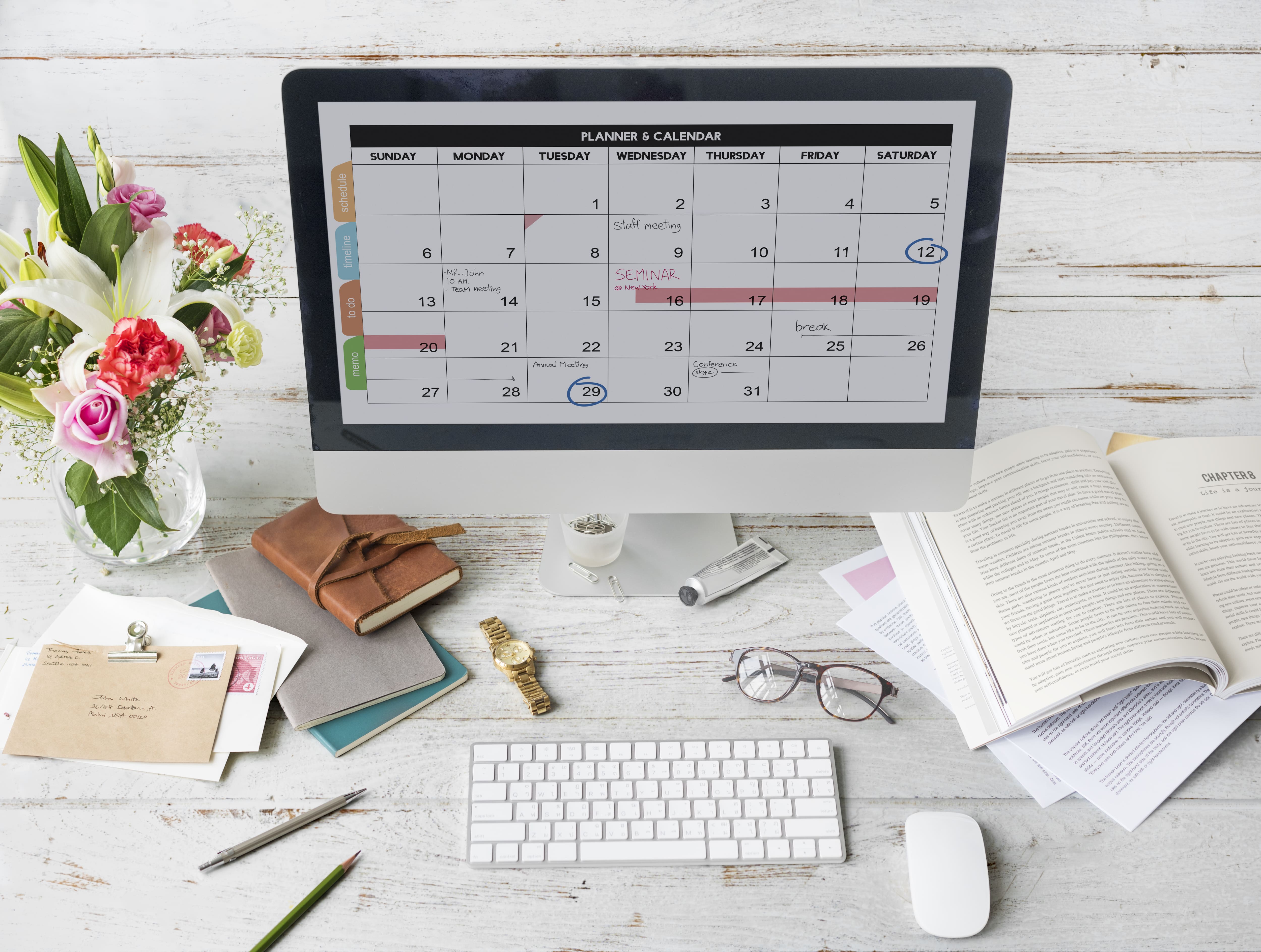 Bildbeschreibung: Digitaler Kalender auf Schreibtisch mit Blumen und Notizbüchern für effizientes Zeitmanagement.