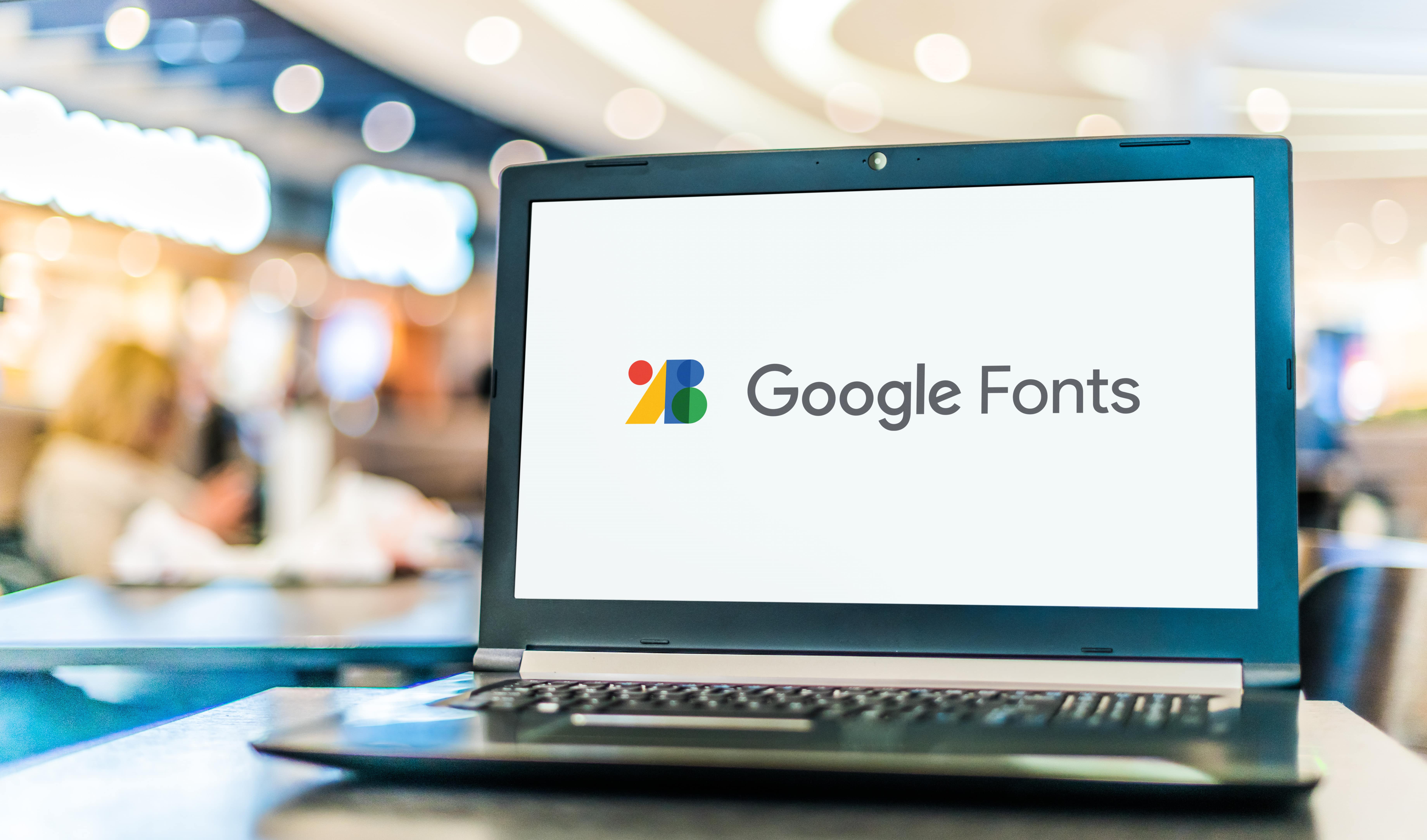Laptop mit Google Fonts-Logo im Café, Thema: Optimierung von Webdesign mit Google-Schriften.