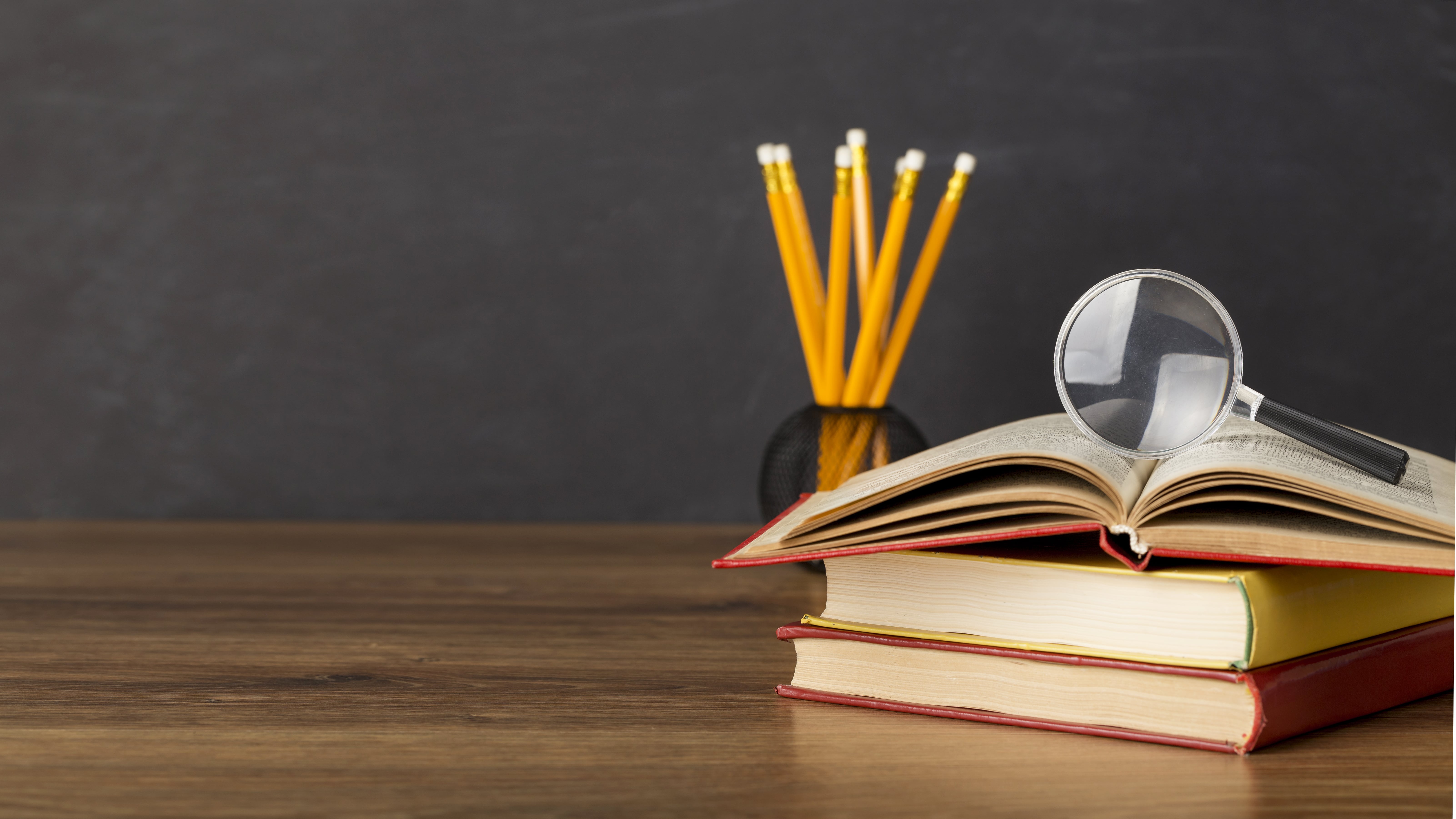 Bücherstapel mit Lupe und Stiften; Thema: effektive Lerntechniken und Recherchemethoden für Studenten.